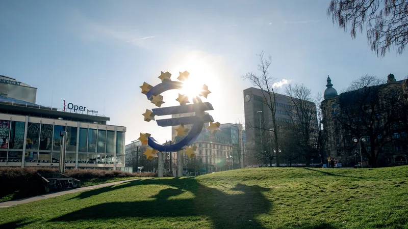 Euro sculpture in Frankfurt, Germany with cityscape buildings and sunlight.