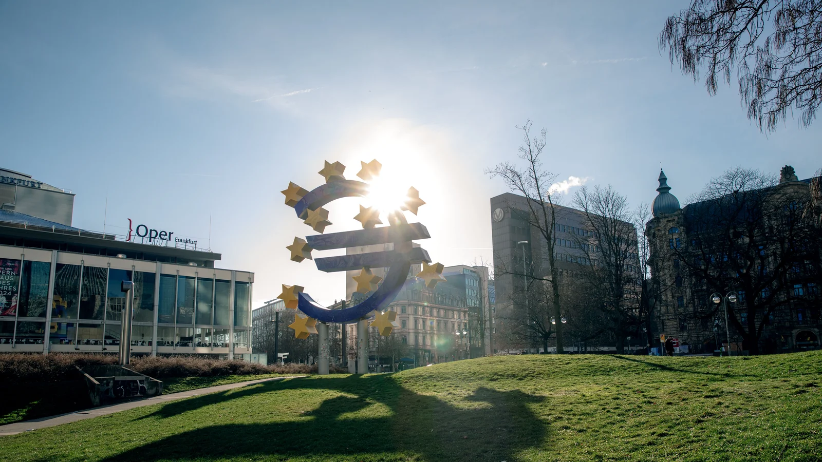Euro sculpture in Frankfurt, Germany with cityscape buildings and sunlight.